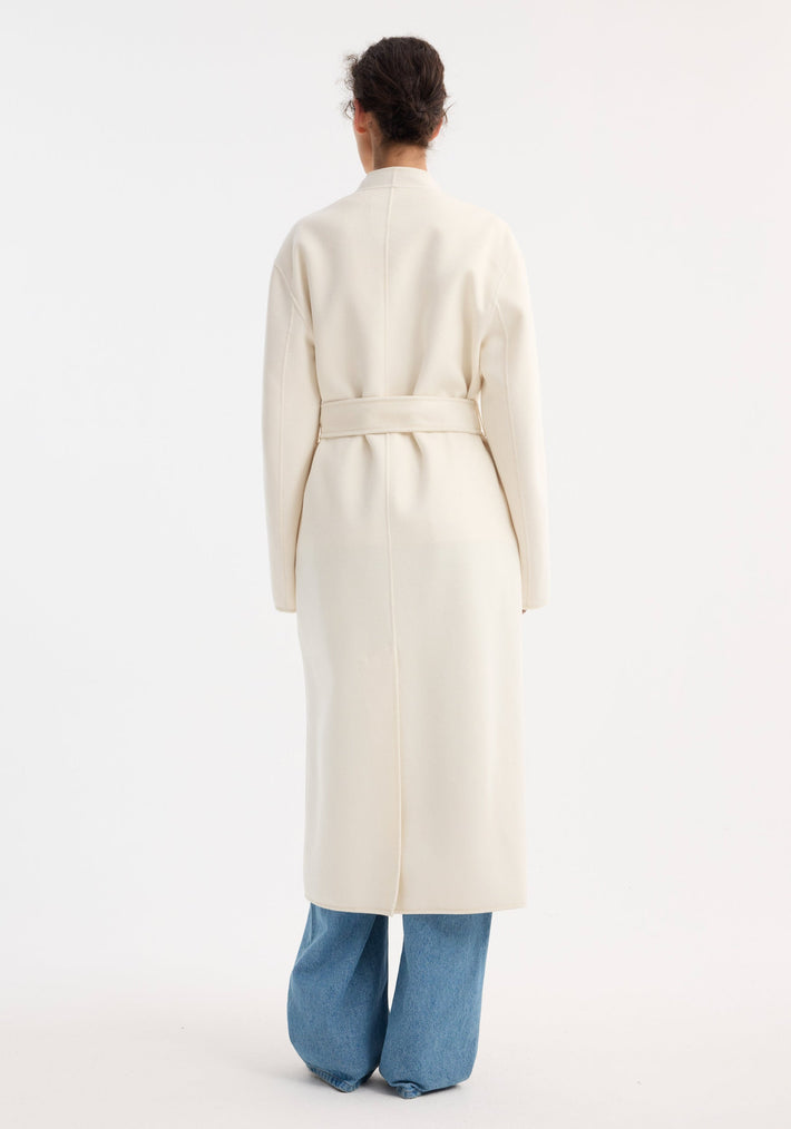 Back view of a person wearing the Double-faced kimono style coat in off white, featuring a self-tie belt and patch pockets, over light-blue jeans.