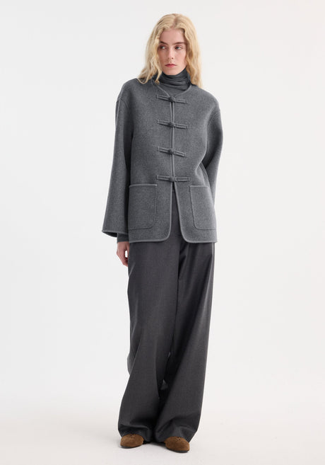 Model in a minimalist grey ensemble featuring the Róhe 'Marie' mandarin double-faced wool jacket with pankou closure, embroidered edges, and patch pockets.