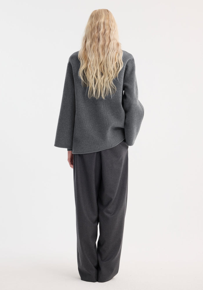 Person wearing a mid grey melange Mandarin double-faced wool jacket with embroidered edges, patch pockets, and pankou closure, seen from behind, showcasing its loose-fitting design.