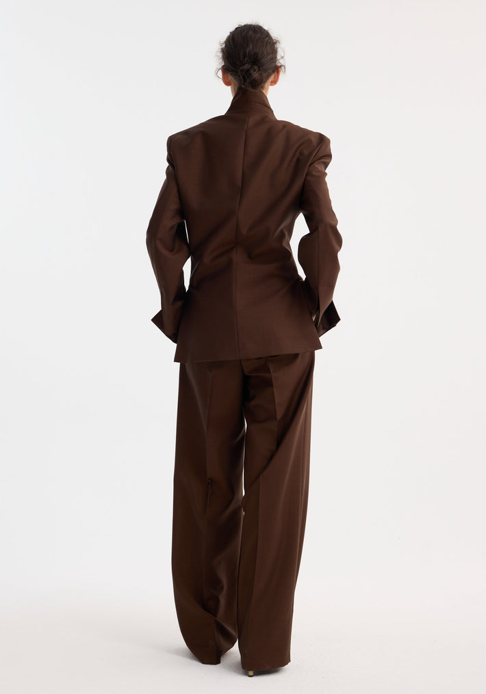 Person wearing Dual tone piqué overlap suit jacket in mahogany, featuring an oversized blazer and wide-leg trousers, standing against a plain studio background.