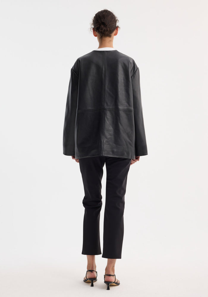 Person wearing the Róhe 'Marie' Mandarin leather jacket with pankou closures and patch pockets, paired with slim black pants and low-heel sandals.