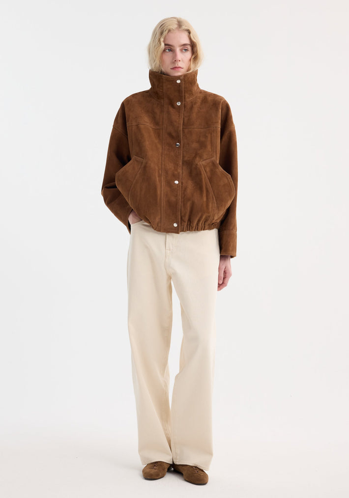 Model wearing a Reinvented suede jacket in cognac with a cropped, high-collar design, oversized pockets, paired with cream denim trousers and matching suede shoes.