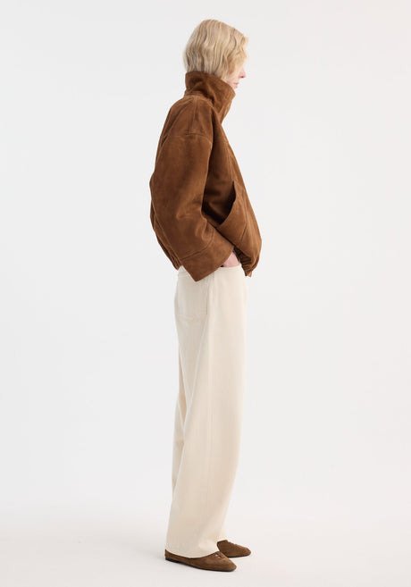 Model wearing a Reinvented suede jacket in cognac with a cropped, high-collar design, oversized pockets, paired with cream denim trousers and matching suede shoes.