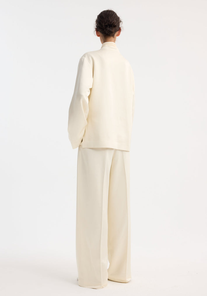 Person wearing Mandarin pearl button satin jacket with mandarin collar, front patch pockets, paired with matching wide-leg trousers. Hair in a simple bun.