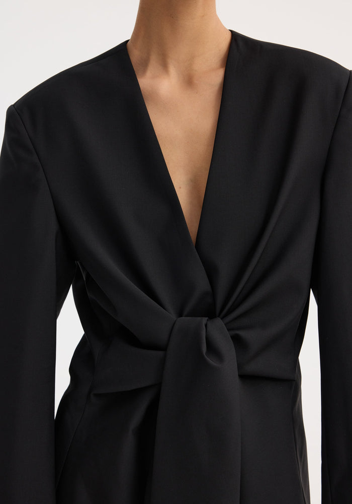 Person wearing a Sleeve-cinched blazer-top | black, featuring a deep V-neckline and waist twist for a tailored look. Made from virgin wool and wool mohair blend.