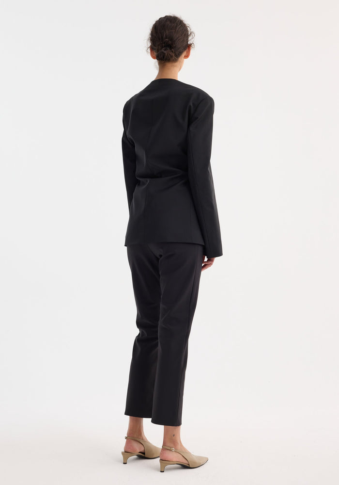 Rear view of a model in a Sleeve-cinched blazer-top | black, featuring a tailored fit with cinched sleeves and wrap waist, paired with matching trousers and beige slingbacks.
