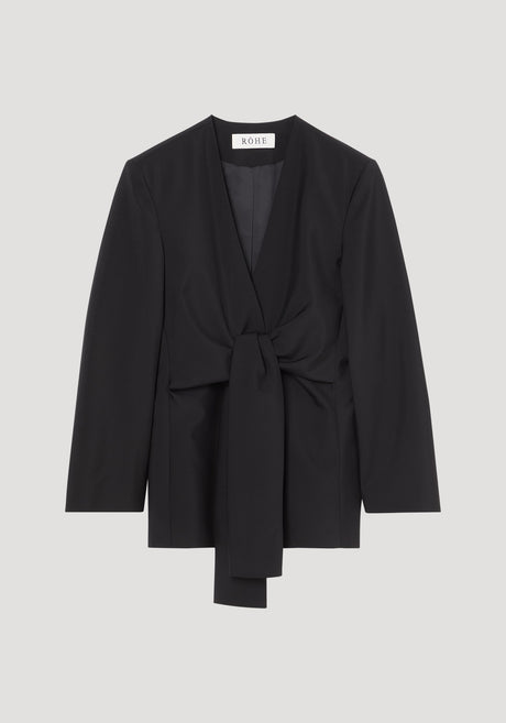 Sleeve-cinched blazer-top in black with deep V-neck and self-tie waist; combines tailoring structure with elegant wrap design. Brand label “RÓHE” visible at back neck.