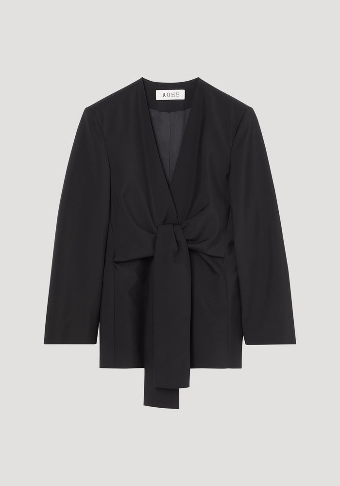 Sleeve-cinched blazer-top in black with deep V-neck and self-tie waist; combines tailoring structure with elegant wrap design. Brand label “RÓHE” visible at back neck.
