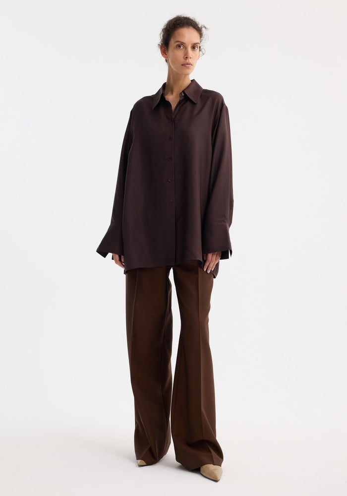 Model wearing Deconstructed silk shirt | mahogany, featuring an open back and tie detail, paired with matching wide-leg trousers and tan pointed-toe heels.