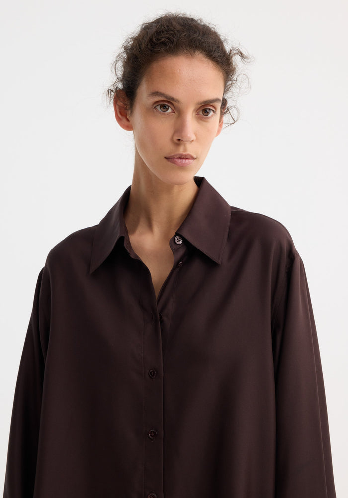 Close-up of a person wearing a Deconstructed silk shirt | mahogany, showcasing its open back and versatile tie detail for varied styling.