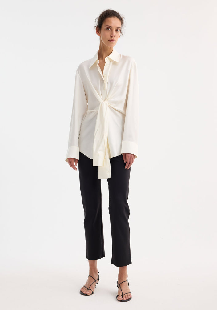 Silk knotted shirt | cream: Cream-colored, long-sleeve blouse with a pointed collar, featuring a unique twisted knot design at the waist for a draped effect.