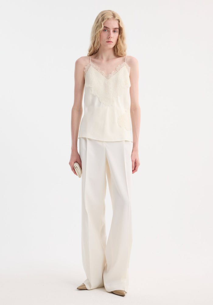 Tall person models Lace camisole | cream with v-neck, lace trim, and adjustable straps, paired with high-waisted trousers, showcasing minimalist elegance.