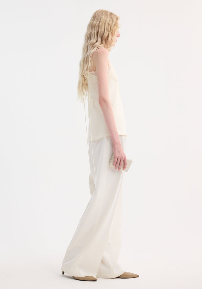 Lace camisole in cream with v-neck, lace trim, adjustable straps; worn with wide-leg trousers and low-heel shoes, held with a light clutch.