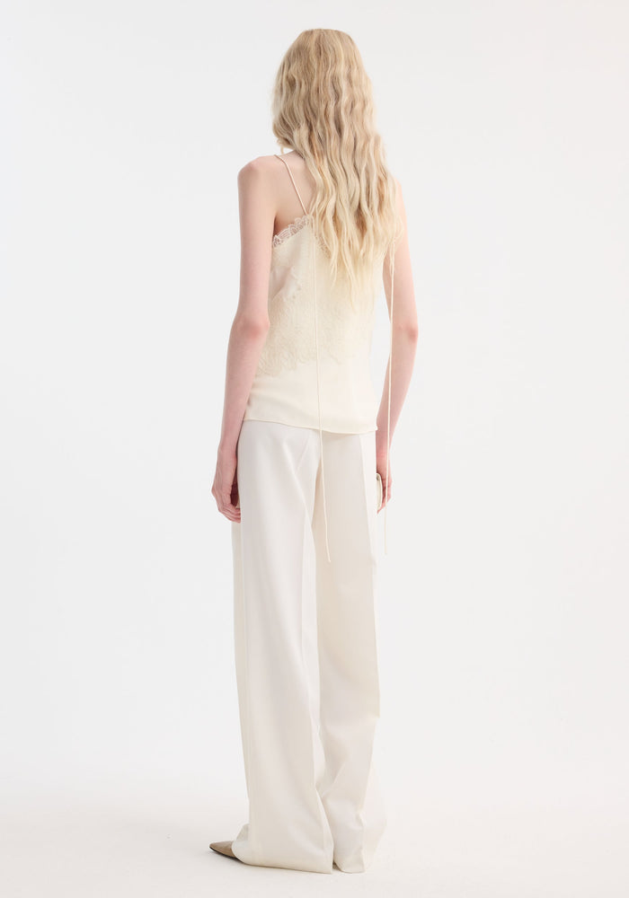 Lace camisole | cream: Tall figure in a lace-trimmed, v-neck camisole with adjustable straps, paired with wide-leg trousers, holding a clutch.