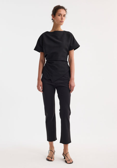 Draped lapel top | black features a boat neckline, flared sleeves, twisted waist drape, and asymmetrical hem, embodying minimalist, architectural design.