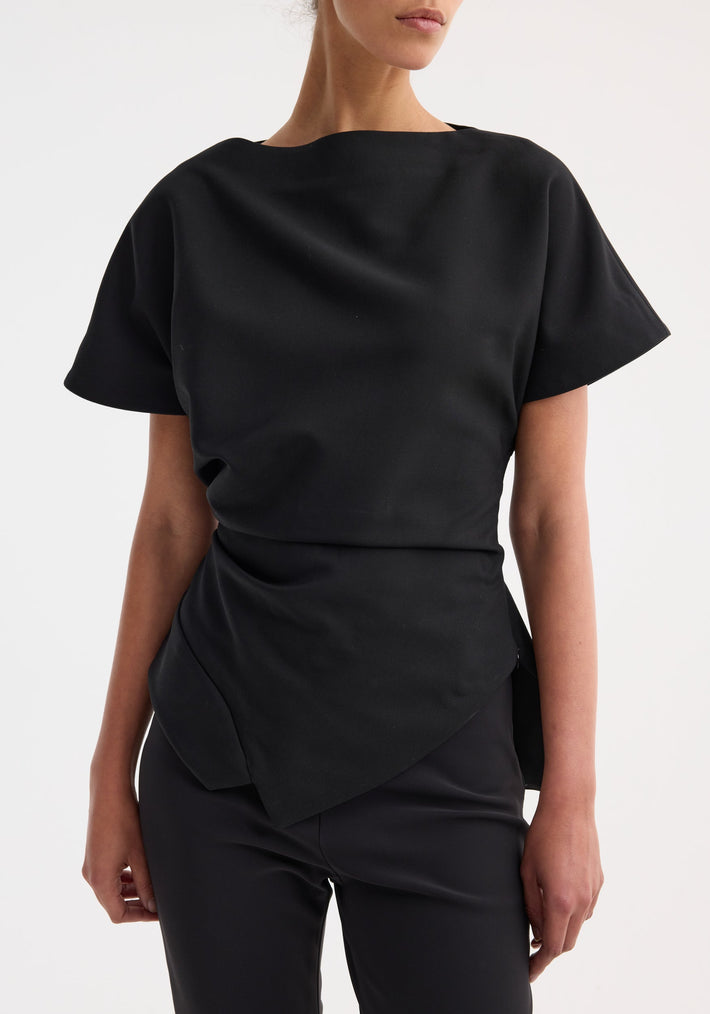 Draped lapel top | black features a sculptural asymmetrical silhouette with a boat neckline and wrapped hem, worn with slim-fit trousers.