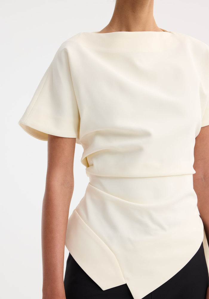 Draped lapel top in off-white with an asymmetrical, pointed hem. Features a wide neckline, dolman sleeves, and fitted waist, showcasing architectural tailoring.