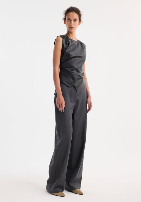 Sleeveless draped leather top in black with asymmetric layered hem, rounded neckline, fitted waist, and center-back zipper, offering a modern elegant silhouette.