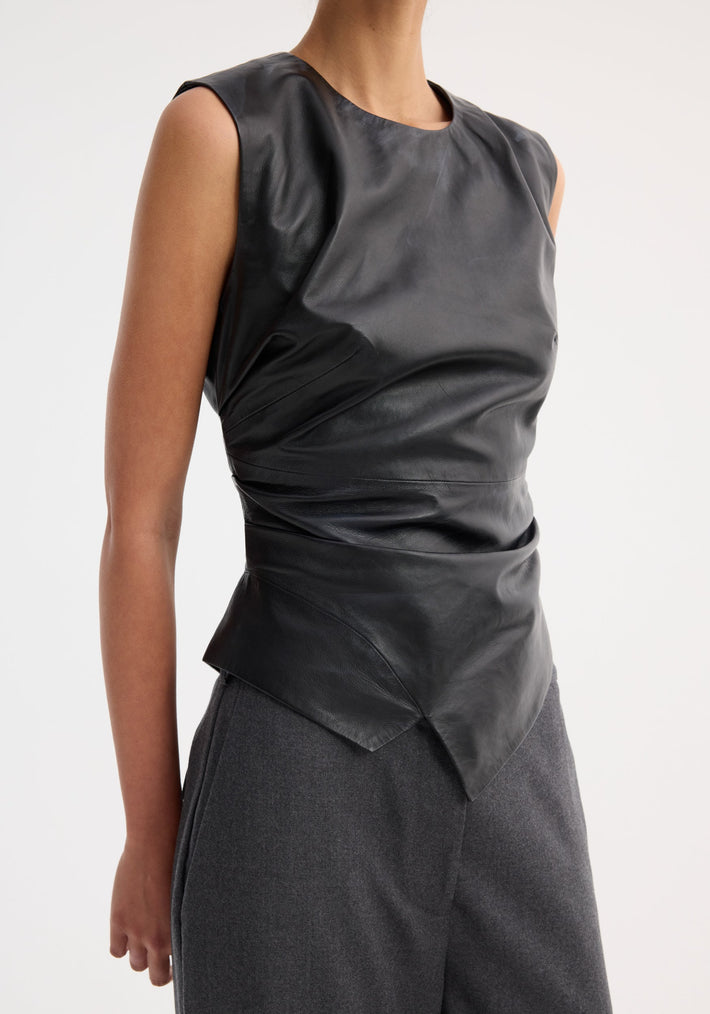 Sleeveless draped leather top in black, featuring an asymmetrical, deconstructed lapel and form-fitting design, paired with charcoal-gray trousers.