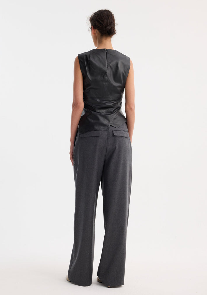 Back view of a person in a sleeveless draped leather top with asymmetrical, deconstructed lapel and fitted waist, paired with high-waisted, wide-leg trousers.