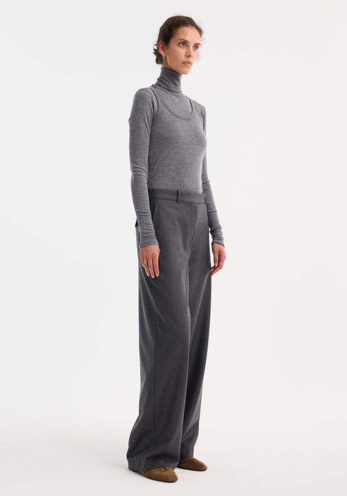 Woman wearing Double-layer wool top in mid grey melange, featuring a fitted turtleneck and tank, paired with wide-leg trousers and brown suede flats.