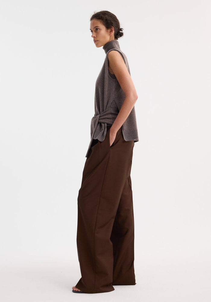 Woman in a Double-layered knit top, mud melange, with a fitted turtleneck and casual sweater at waist, paired with wide-leg trousers and flat sandals.