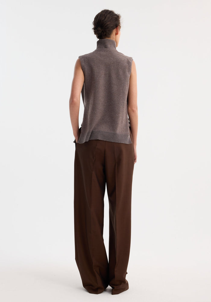Model wearing Double-layered knit top | mud melange, showcasing a deconstructed design with tie-sleeve details and a wide-leg trouser ensemble against a plain backdrop.
