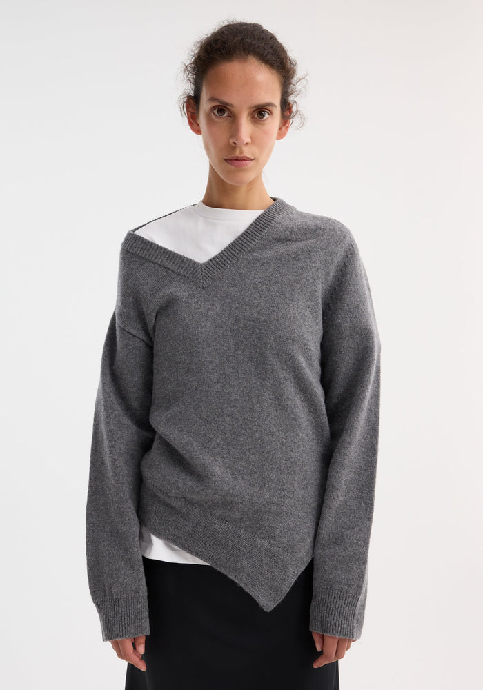 Woman modeling the Two-way deconstructed jumper in mid grey melange, featuring a relaxed fit, asymmetrical hem, and versatile V-neck over a white T-shirt.
