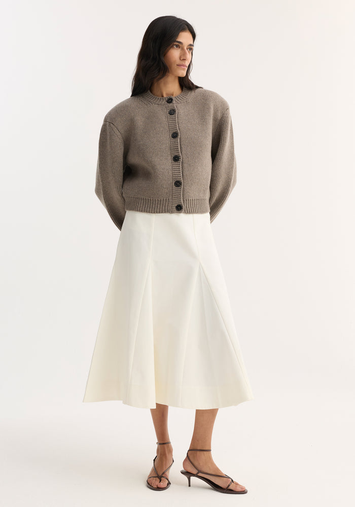 Woman wearing the Statement Shoulder Cardigan in clay melange, showcasing its chunky knit, oversized fit, and large dark buttons, paired with a high-waisted midi skirt.