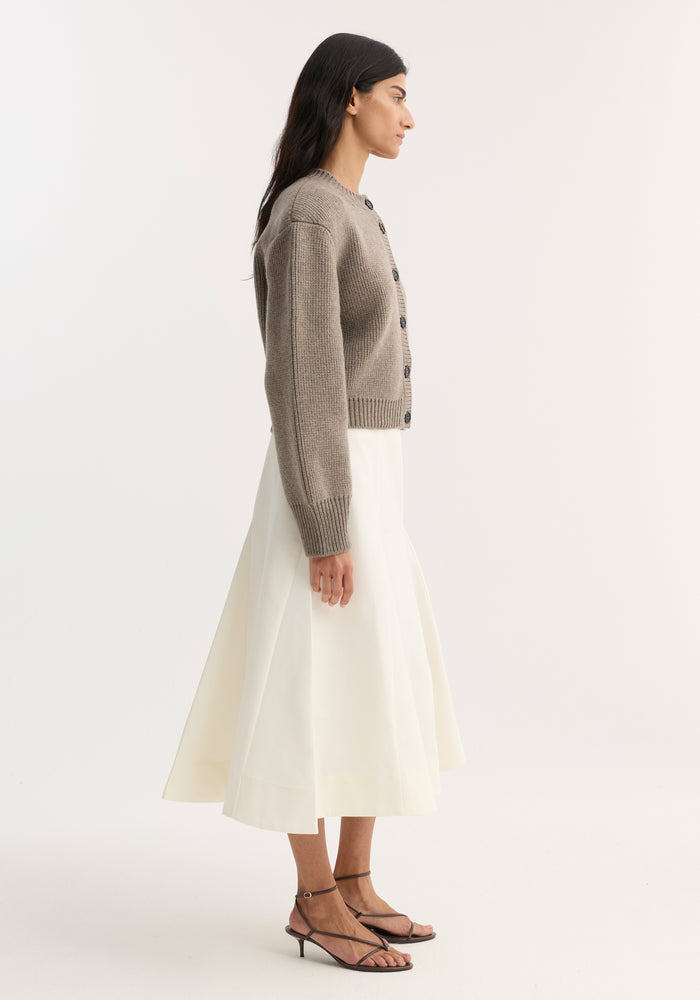 Model wearing Statement Shoulder Cardigan | Clay Melange, showcasing its oversized fit and structured shoulders, paired with a cream midi skirt and dark strappy sandals.