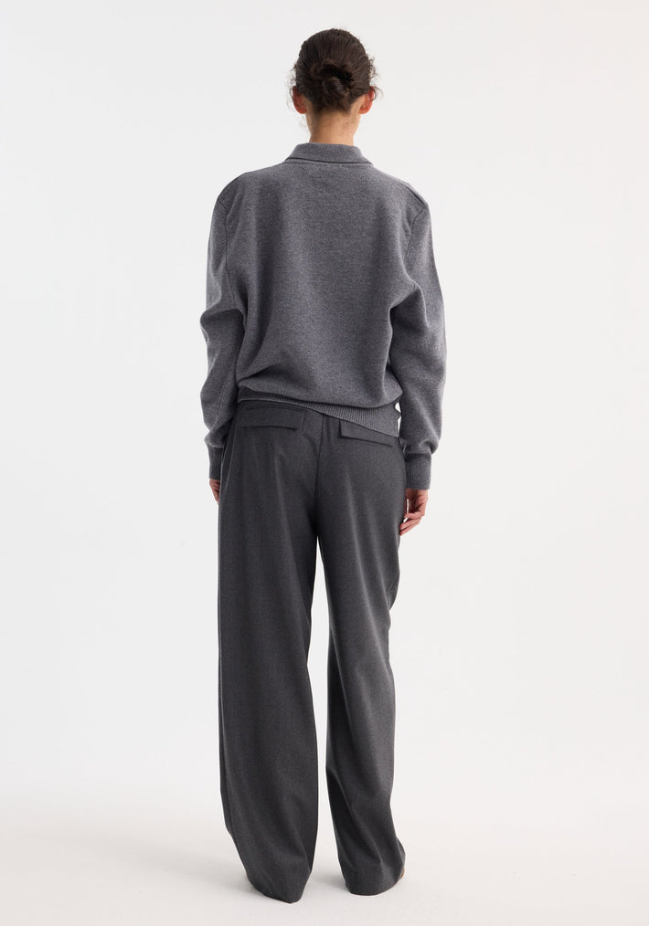 Person wearing a Compact knitted polo in mid grey melange, with ribbed cuffs and collar, paired with wide-leg trousers, hair in a bun, back to camera.