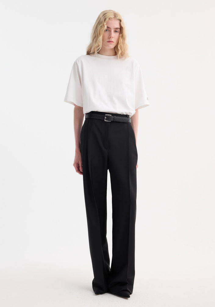 Person in Oversized cotton t-shirt, optic white, tucked into high-waisted black trousers, showcasing a relaxed fit with drop shoulder and crew neck.
