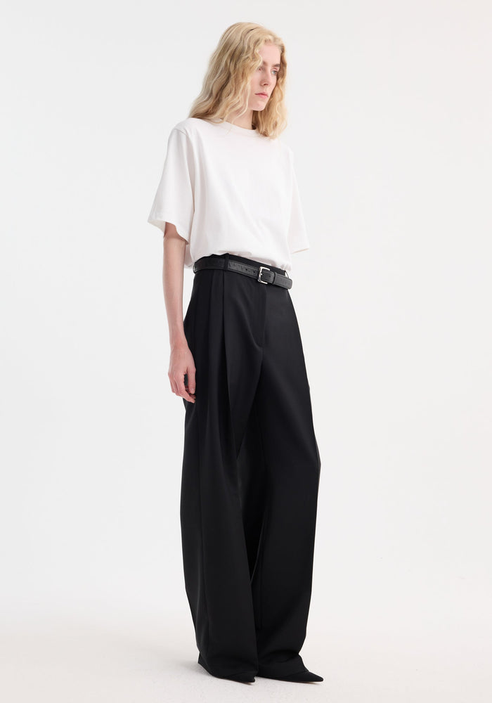 Person wearing Oversized cotton t-shirt in optic white, featuring a relaxed fit and drop shoulders, paired with high-waisted wide-leg black trousers.