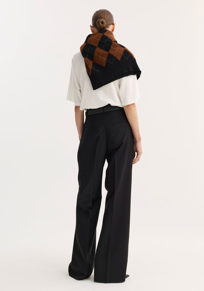 Back view of a model wearing black mid-waist tailored trousers, featuring a wide leg and slim belt, draped with a check-patterned knit sweater.