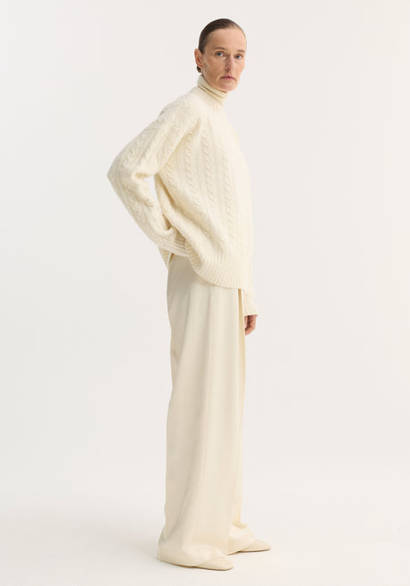 Model wearing Relaxed drawstring satin trousers in cream, featuring a wide-leg fit and drawstring waistband, paired with a chunky cable-knit sweater.