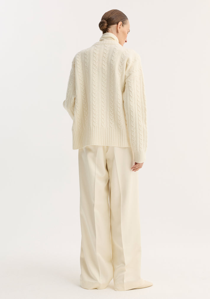 Woman in chunky sweater with relaxed drawstring satin trousers, showcasing wide-leg silhouette and tailored elegance, hair in a low bun.