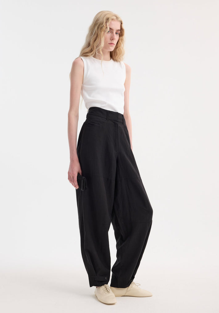 Model wearing Parachute trousers | black, high-waisted with wide legs, tailored waistband; paired with a sleeveless top and oxford shoes, holding a black clutch.