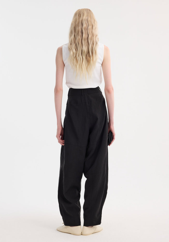 Back view of a person wearing Parachute trousers | black, showcasing high-waisted, wide-leg design in viscose-linen blend, paired with a white sleeveless top.