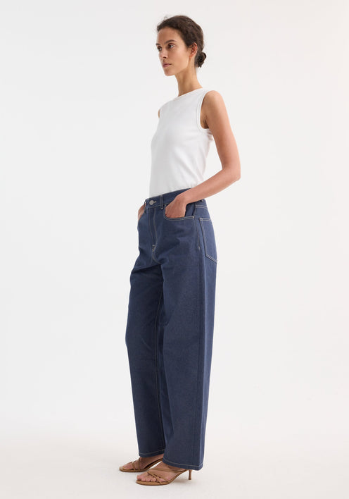 Woman wearing Signature baggy fit raw denim jeans with a low-waist, wide-leg design and a ribbed tank top, styled with tan heeled sandals.