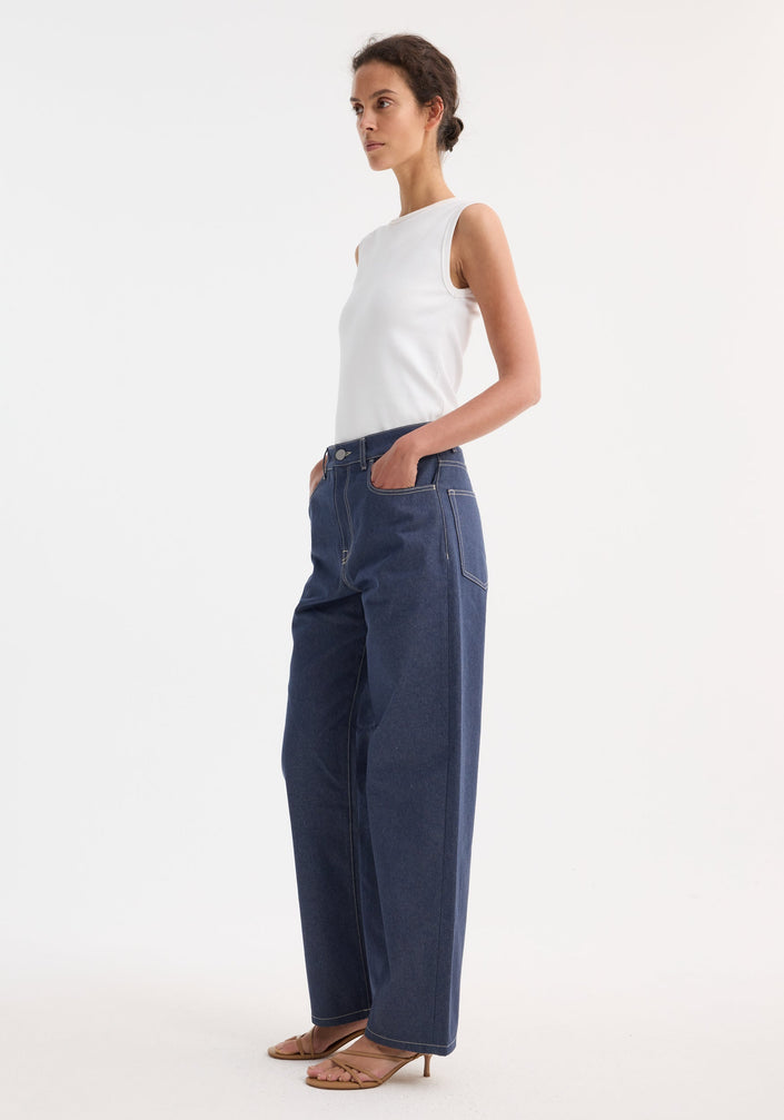 Woman wearing Signature baggy fit raw denim jeans with a low-waist, wide-leg design and a ribbed tank top, styled with tan heeled sandals.