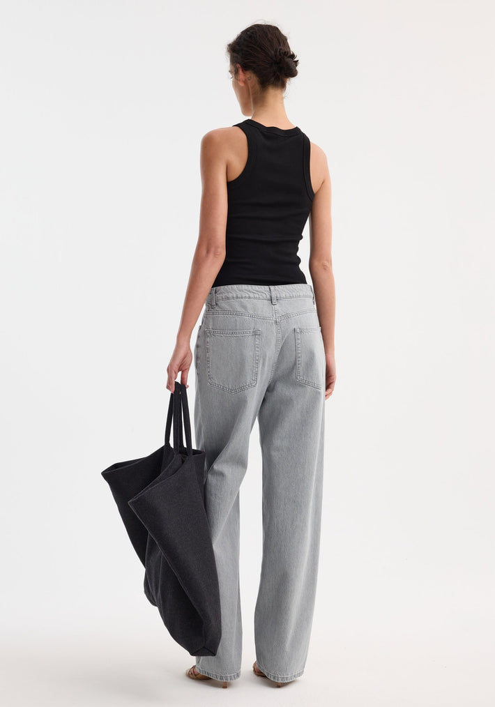 Woman in fitted black tank top and Signature baggy fit denim | washed grey, holding a slouchy black tote, hair in a low bun, wearing sandals.