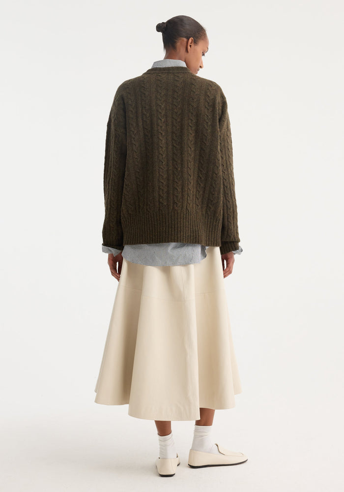 A-line leather skirt in chalk, featuring a voluminous silhouette with croco embossing, worn below a checkered shirt and cable-knit sweater.