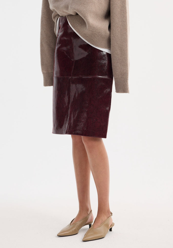 Model wearing the Snake leather skirt | burgundy snake, a high-waist, knee-length, burgundy pencil skirt with a snake-skin texture, paired with tan slingback heels.