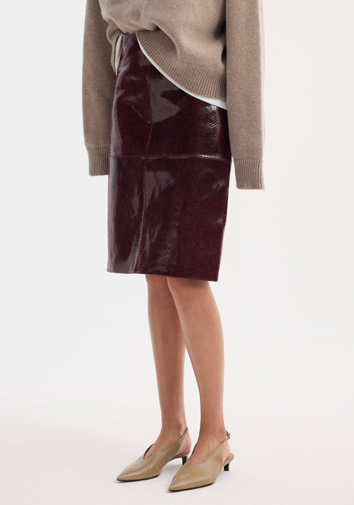 Model wearing the Snake leather skirt | burgundy snake, a high-waist, knee-length, burgundy pencil skirt with a snake-skin texture, paired with tan slingback heels.