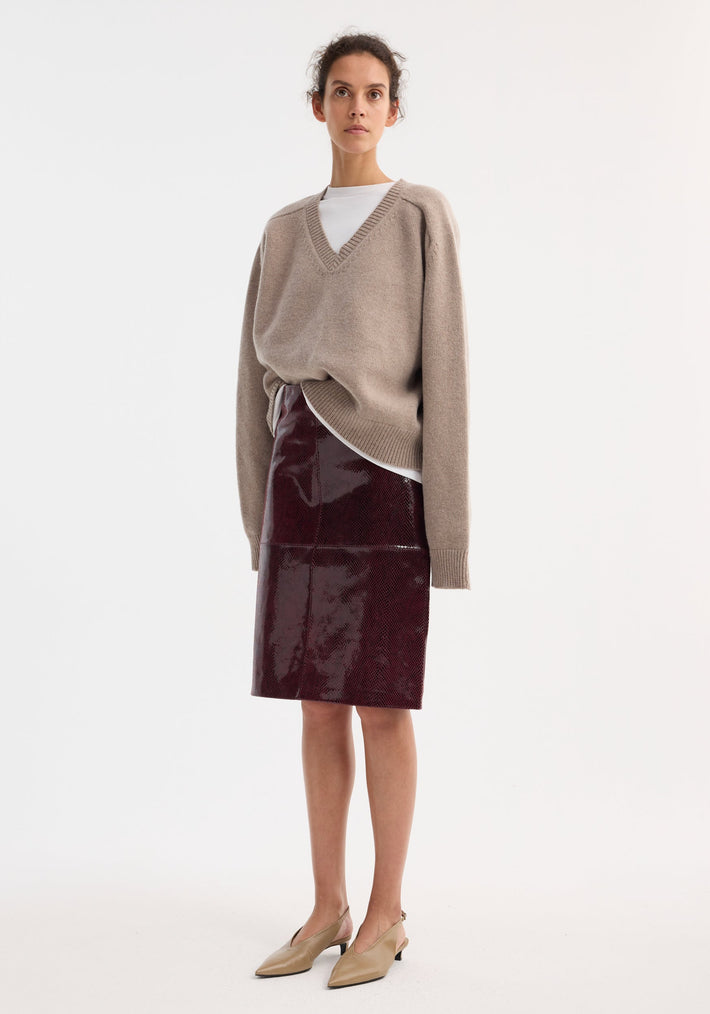 Young woman wears a burgundy snake leather skirt paired with a light taupe V-neck sweater and beige slingback pumps, showcasing the skirt's embossed texture and sleek fit.