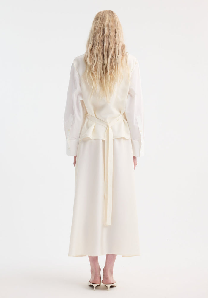 Back view of a person in a Poplin silk combined gilet-dress featuring a deconstructed design with open armholes and a flowing ankle-length silhouette.