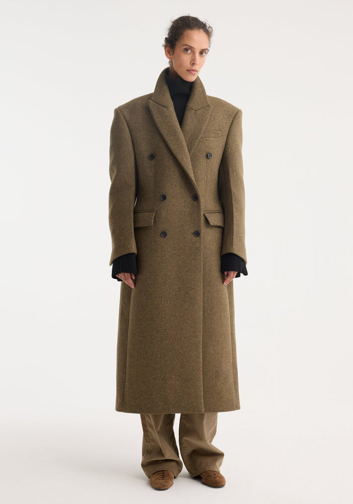 Hourglass wool coat in forest melange, featuring a double-breasted design, notched lapels, broad shoulders, and flap pockets, paired with a black turtleneck and tan trousers.