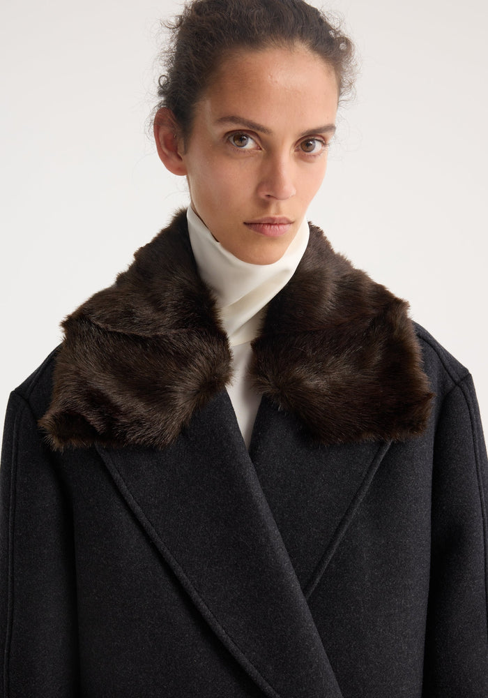 Model wearing Double-breasted coat with faux fur collar in anthracite melange, showcasing a tailored wool silhouette with an oversized, dark brown faux-fur collar.