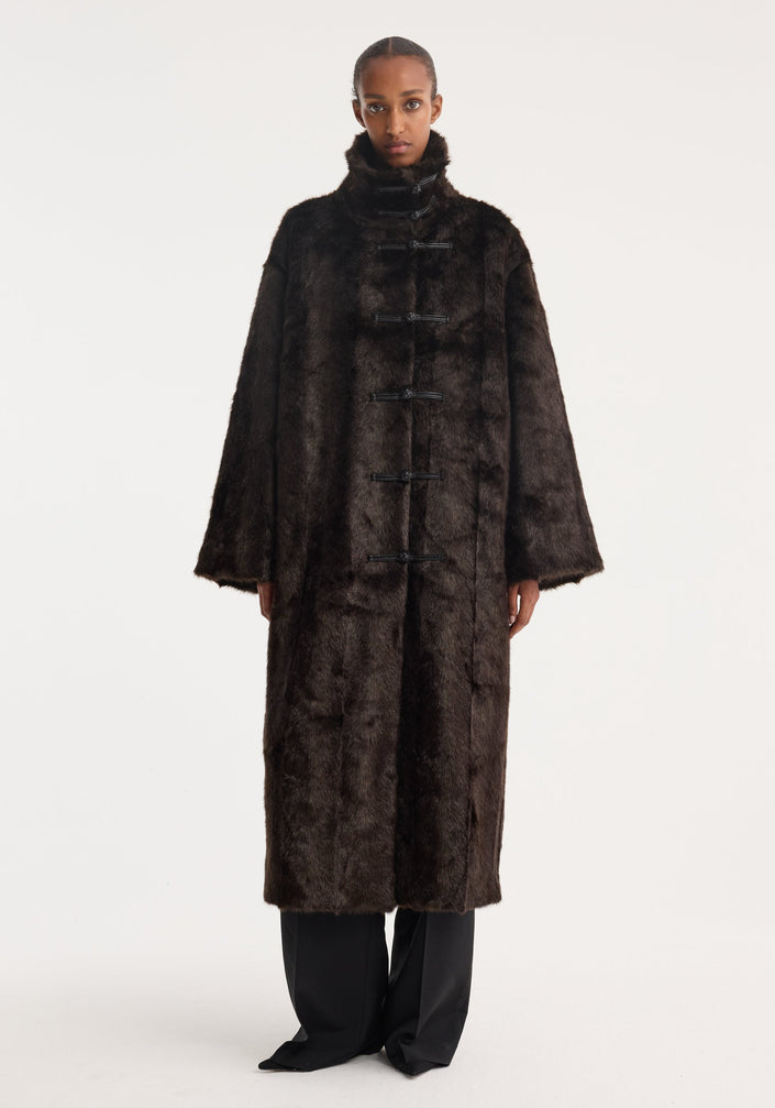 Mandarin faux fur coat in dark brown with a full-length design, stand-up collar, and five toggle-style closures, modeled in an oversized fit.