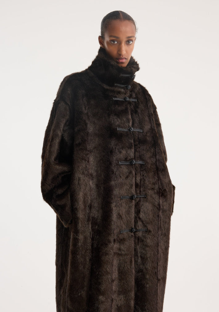 Model wears a Mandarin faux fur coat in dark brown, showcasing its oversized fit, stand-up collar, and signature mandarin toggle closures.